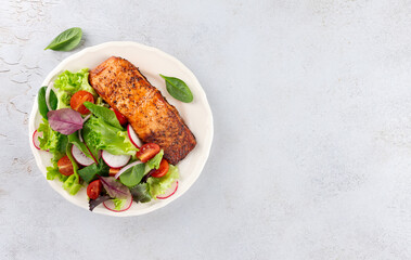 Grilled salmon fillet with fresh leafy greens, cherry tomatoes, radish on white background. Top view