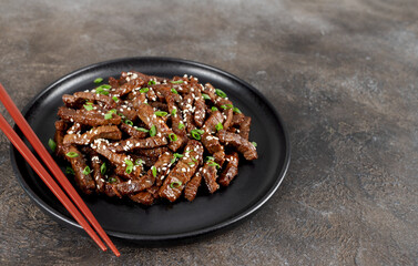 Fried teriyaki beef with sesame seeds and green onions on a brown background. Asian cuisine.