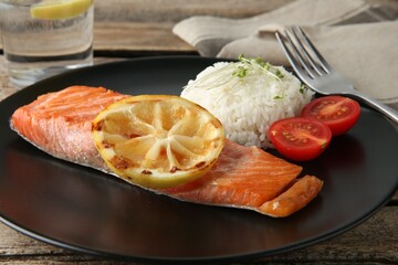 Piece of tasty grilled salmon, lemon, tomato, rice and microgreens on wooden table, closeup