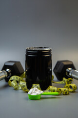 Fitness supplement jar with green scoop and protein powder, accompanied by dumbbells and measuring tape, illustrating a commitment to health and fitness goals