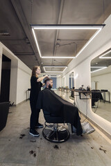Woman Barber making customer Fashionable haircut in Modern style barbershop. Male hair cutting with scissors. Bearded Man client visit gentleman grooming beauty salon for hairstyle care