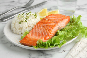 Piece of tasty grilled salmon, lemon, lettuce, rice and microgreens on light marble table, closeup