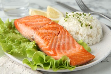 Piece of tasty grilled salmon, lemon, lettuce, rice and microgreens on light marble table, closeup