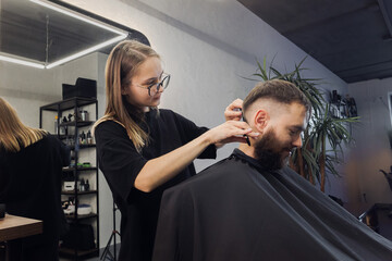 Woman Barber making customer Fashionable haircut in Modern style barbershop. Male hair cutting with scissors. Bearded Man client visit gentleman grooming beauty salon for hairstyle care