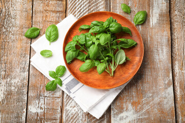 Fresh basil leaves and napkin on color wooden table, flat lay