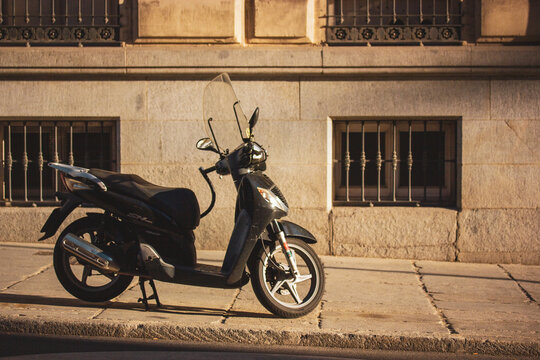 Madrid, Spain 1 June 2024 A black scooter parked on a city sidewalk in front of a building. A sleek scooter is captured in a side view, set against a backdrop of an aged building with barred windows.