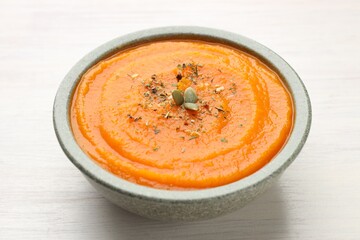Tasty pumpkin cream soup with seeds in bowl on white wooden table, closeup