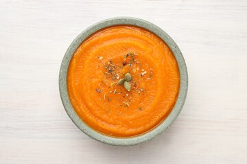 Tasty pumpkin cream soup with seeds in bowl on white wooden table, top view