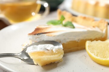 Slice of tasty lemon meringue tart with mint served on table, closeup