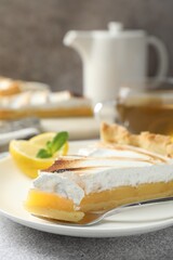 Slice of tasty lemon meringue tart with mint served on light grey table, closeup