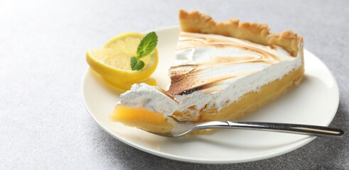 Slice of tasty lemon meringue tart with mint served on light grey table, closeup. Space for text