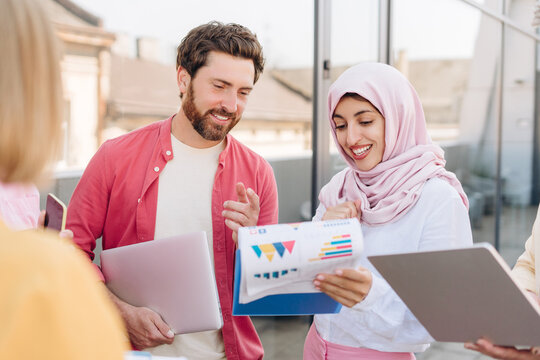 Smiling diverse group of multinational businesswoman wearing hijab and bearded man analyzing graph - Powered by Adobe