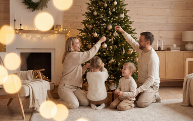 Parents and children decorating Christmas tree in cozy home