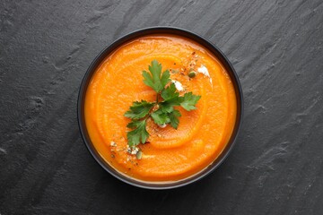 Tasty pumpkin cream soup with parsley in bowl on grey table, top view