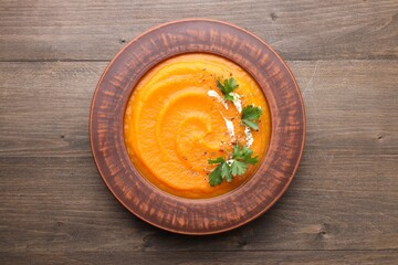 Tasty pumpkin cream soup in bowl on wooden table, top view