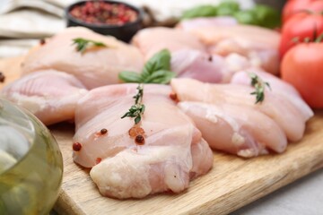 Raw chicken thighs with herbs, peppercorns and tomatoes on light table, closeup