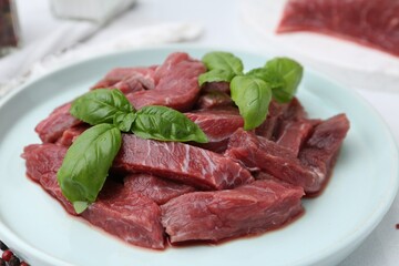 Pieces of raw beef meat and basil on table, closeup