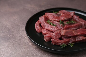 Pieces of raw beef meat and thyme on brown table, closeup. Space for text