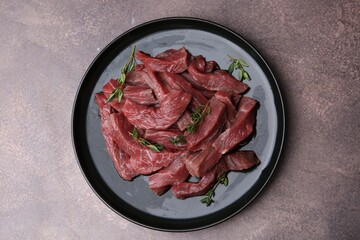Pieces of raw beef meat and thyme on brown table, top view