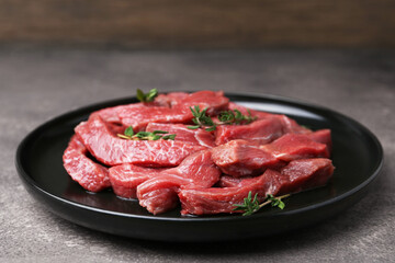 Pieces of raw beef meat and thyme on grey table, closeup