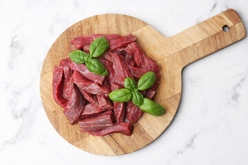 Pieces of raw beef meat and basil on white marble table, top view