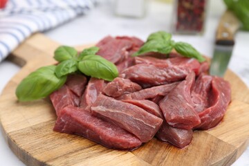 Pieces of raw beef meat and basil on table, closeup