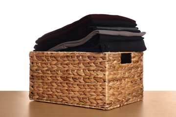 Laundry basket with clean clothes on wooden table against white background