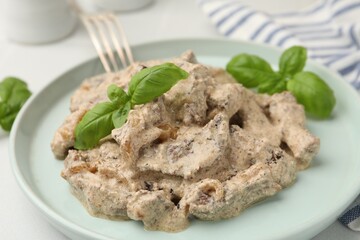 Tasty beef Stroganoff with basil on white table, closeup