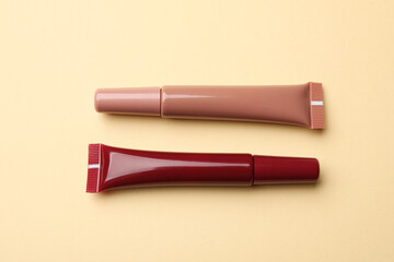 Different lip glosses on beige background, flat lay