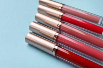 Different lip glosses on light blue background, closeup