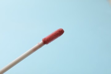 Beautiful lip gloss applicator on light blue background, closeup. Space for text