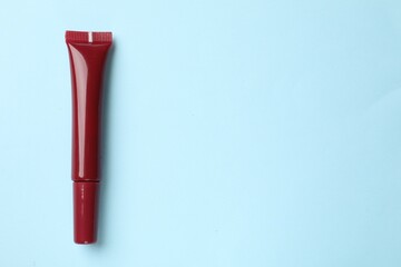 Beautiful dark red lip gloss on light blue background, top view. Space for text