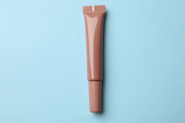 Beautiful nude lip gloss on light blue background, top view