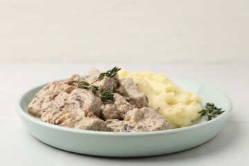 Delicious beef stroganoff with mashed potatoes and thyme on white tiled table, closeup. Space for text