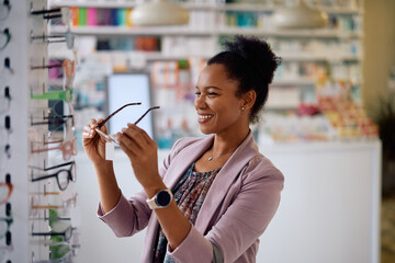 Happy black woman trying on new eyeglasses at optician store.
