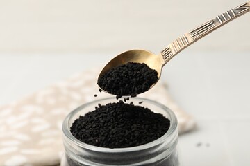 Taking aromatic black caraway with spoon at white table, closeup