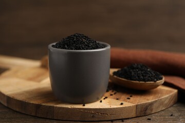 Aromatic black caraway in bowl and spoon on wooden table, closeup