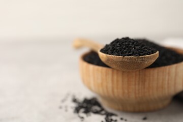Aromatic black caraway in wooden bowl and spoon on light grey table, closeup. Space for text