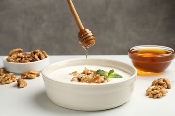 Dripping honey into Greek yogurt with walnuts and mint at white table, closeup