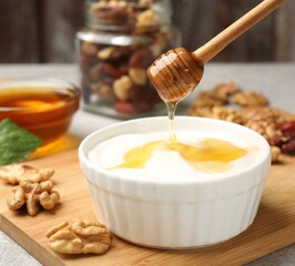 Dripping honey into Greek yogurt and walnuts on grey table, closeup