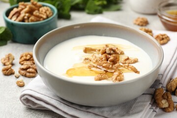Delicious Greek yogurt with honey, nuts and mint on light grey table, closeup