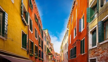 view of narrow street between tall colorful old buildings with open shutters in venice italy