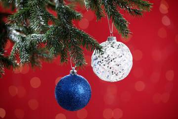 Beautiful balls on Christmas tree branch against red background, closeup. Bokeh effect