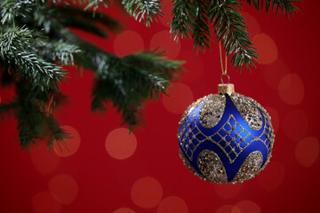 Beautiful ball on Christmas tree branch against red background, closeup. Bokeh effect