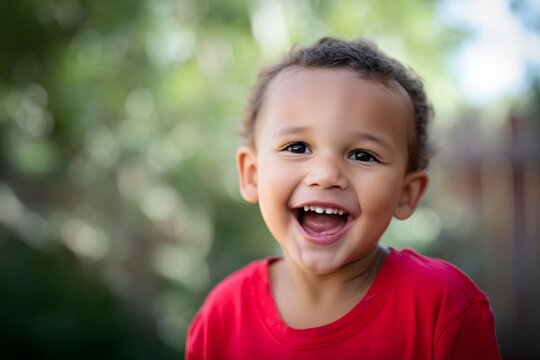 Little boy in a red shirt laughs heartily against an outdoor background