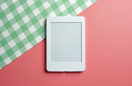 White ebook reader on pink surface near green patterned paper. Device lies on diagonal. Digital book gadget for reading. Reading concept. Modern tech for education or entertainment.
