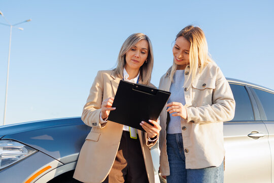 Female instructor explaining driving test details to learner driver near car