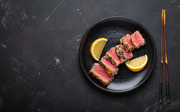 Seared grilled tuna steak tataki slices sesame seeds lemon black plate healthy delicacy space for