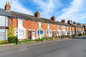 Row of old red brick terraced houses under blue sky with clouds  on a sunny spring day