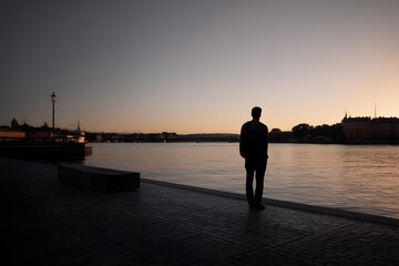 Fototapeta premium Man standing at waterfront watching cityscape at sunset in stockholm, sweden